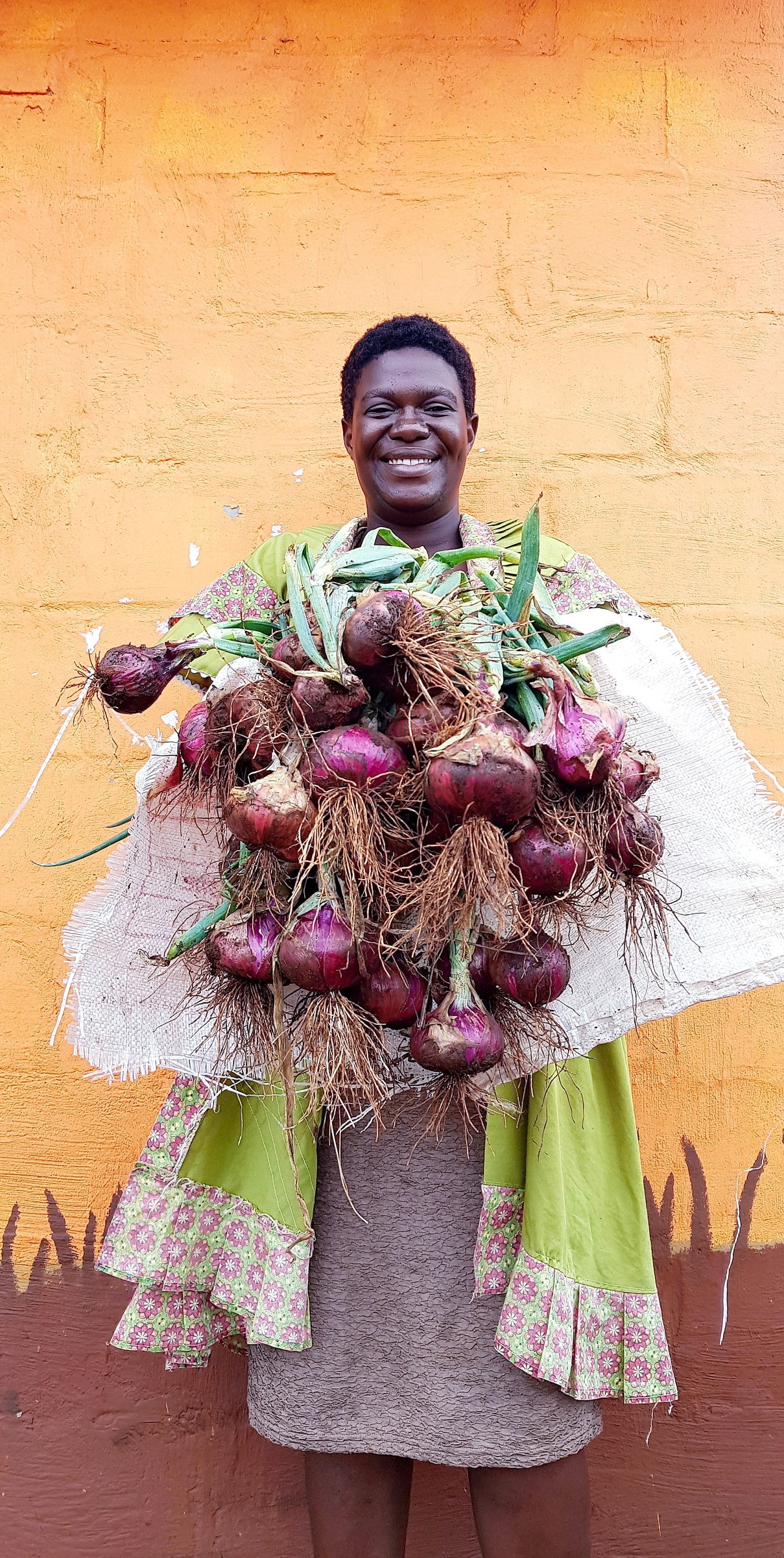 A Mandlakazi participant holding a harvest of red onions in front of a yellow wall