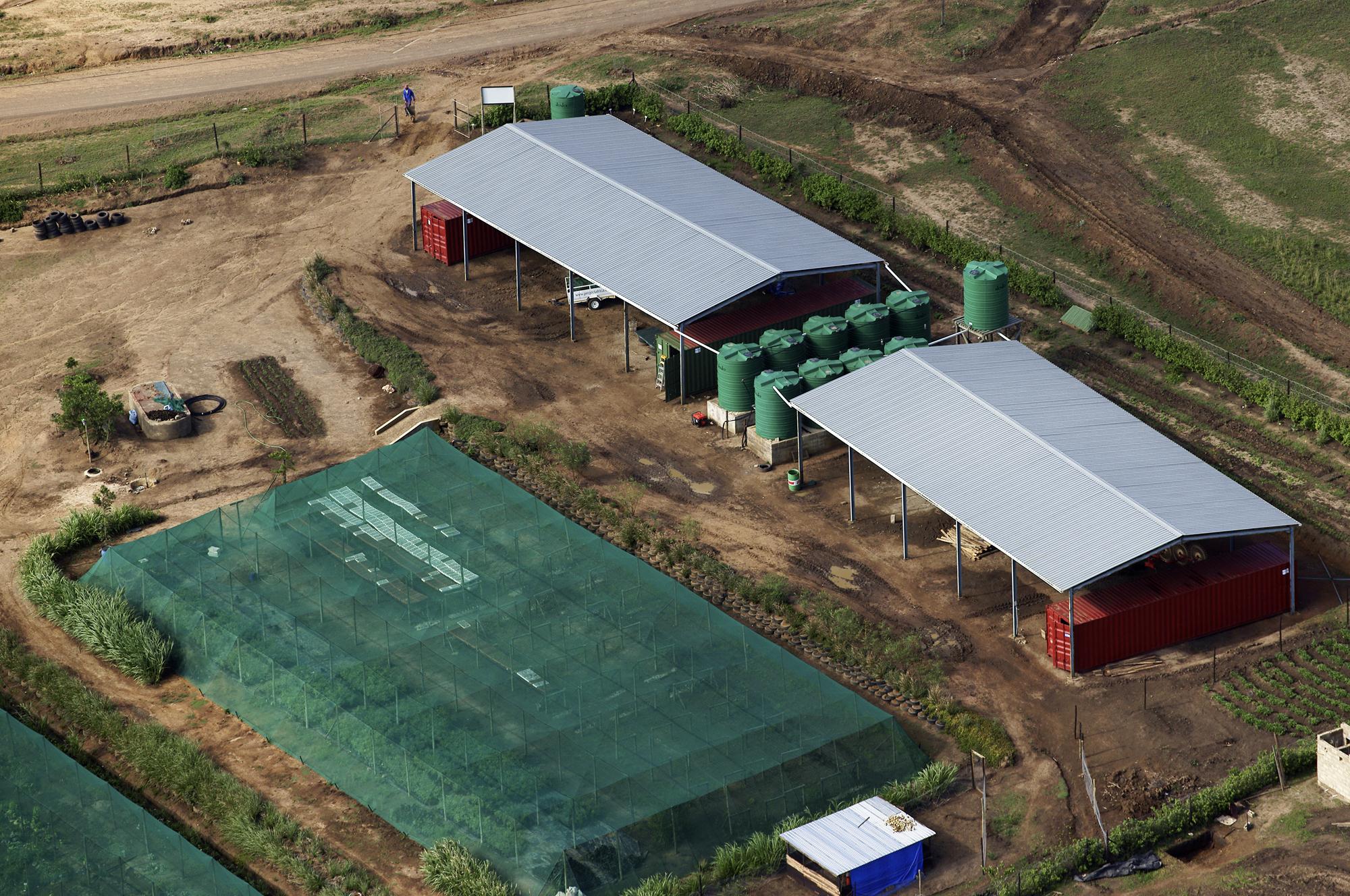 Aerial view of the Mphola Village BioFarm showing shade-net growing areas, rainwater tanks and covered workspaces