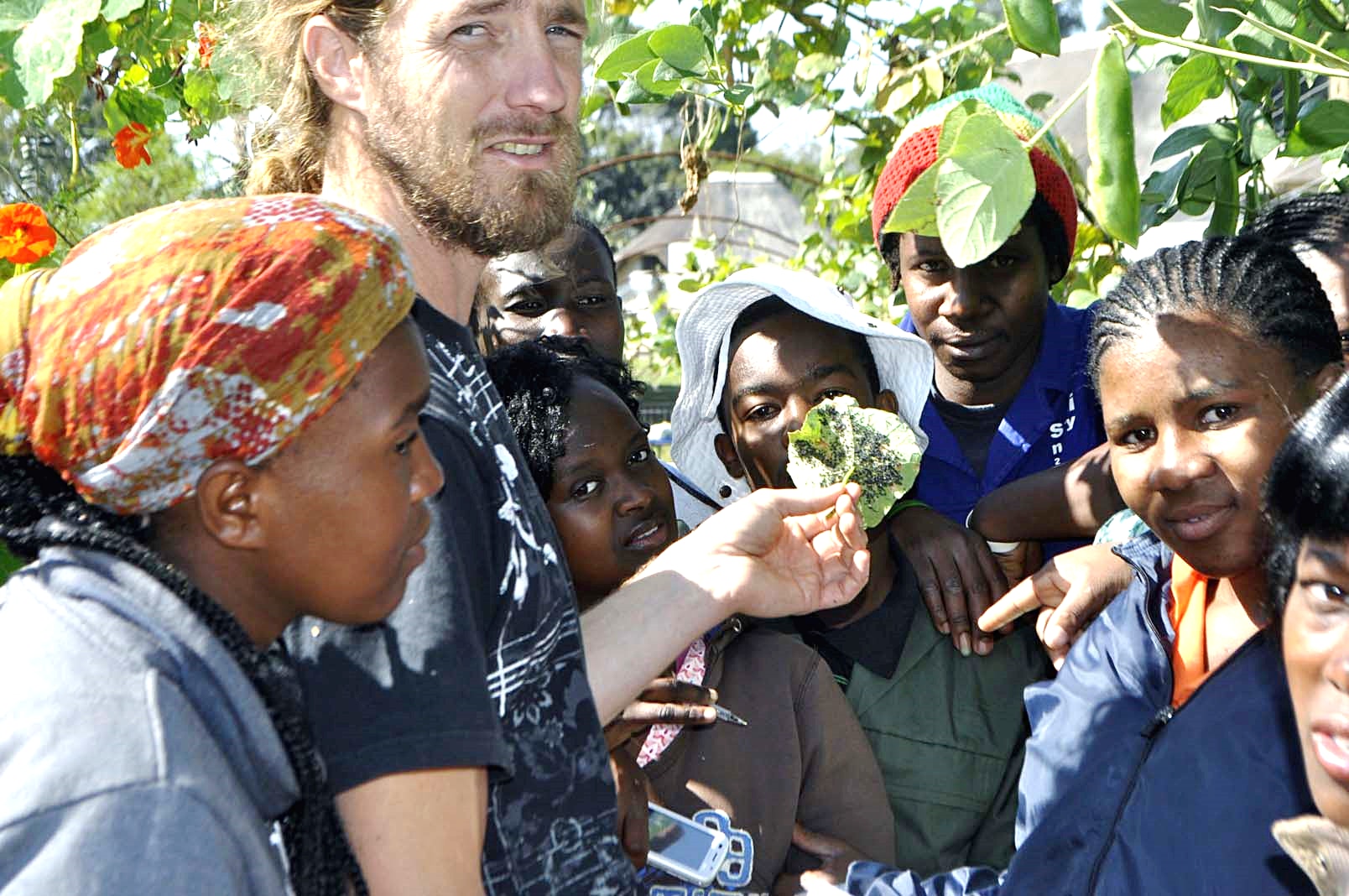 Rory Clark holding up a damaged brassica leaf while a group gathers closely around him in a garden